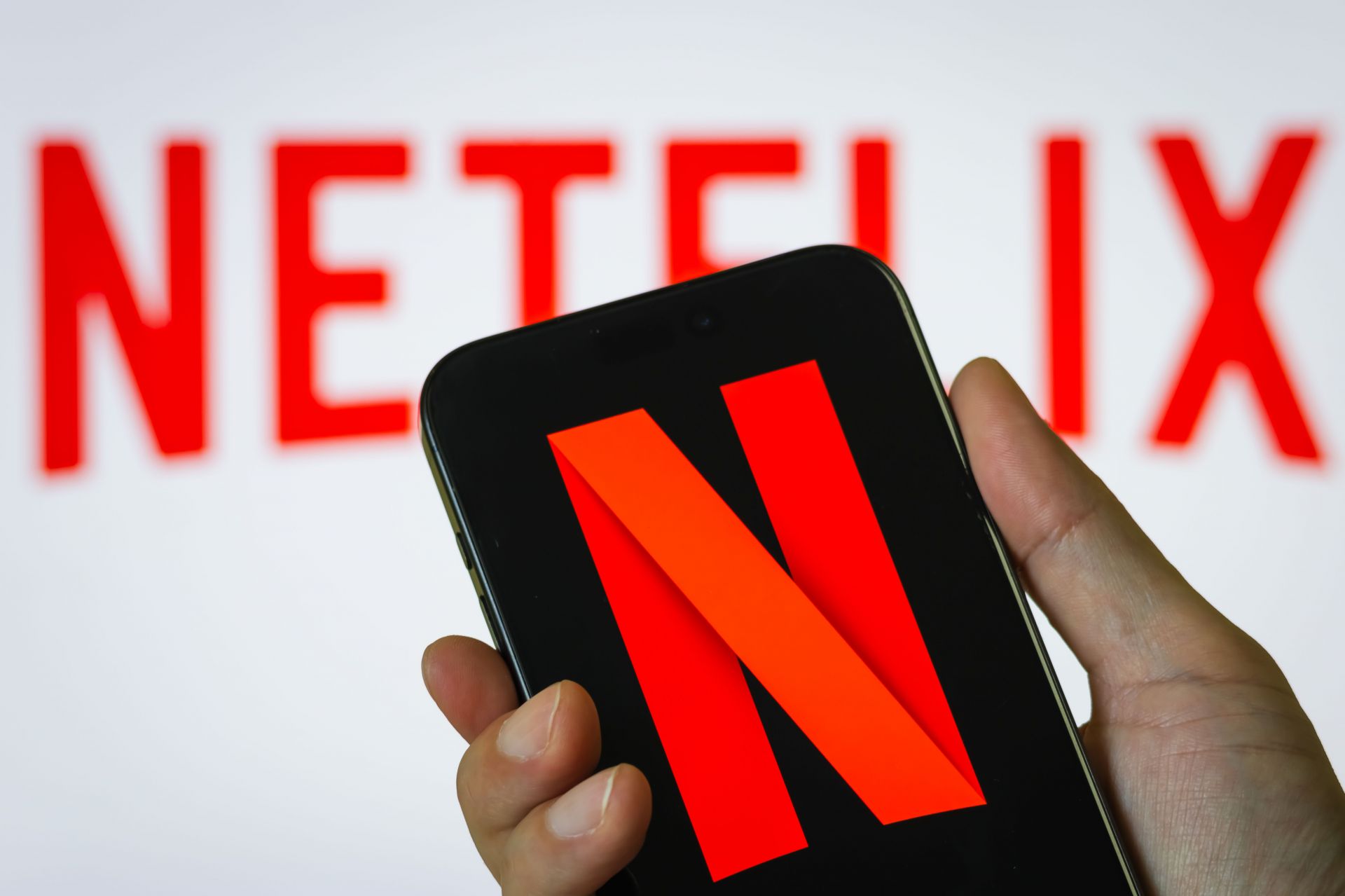 Hand Holding Smartphone Displaying Netflix (NFLX) Logo with Background Branding - Source: Getty