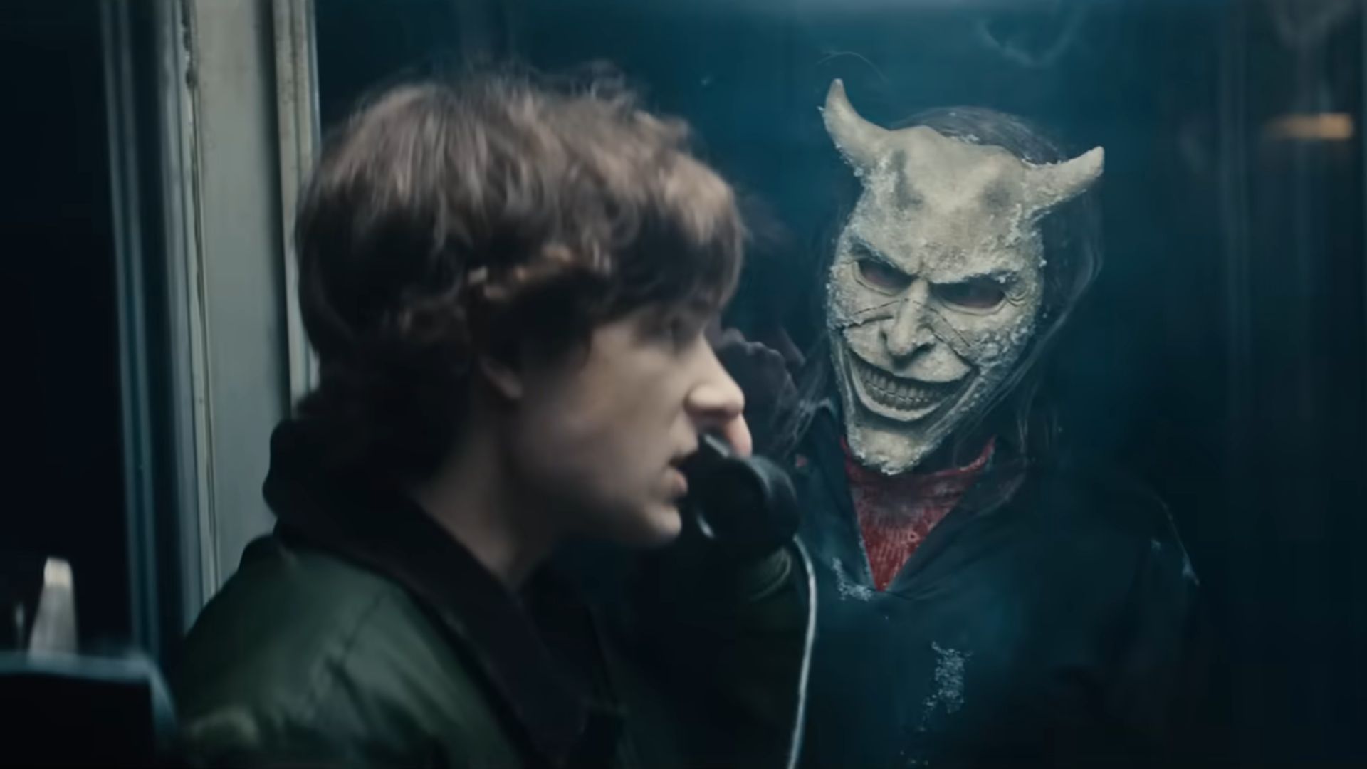 The Grabber (Ethan Hawke) looks at Finney (Mason Thames) from outside a phone booth while Finney stands inside the phone booth and talking to someone on a phone