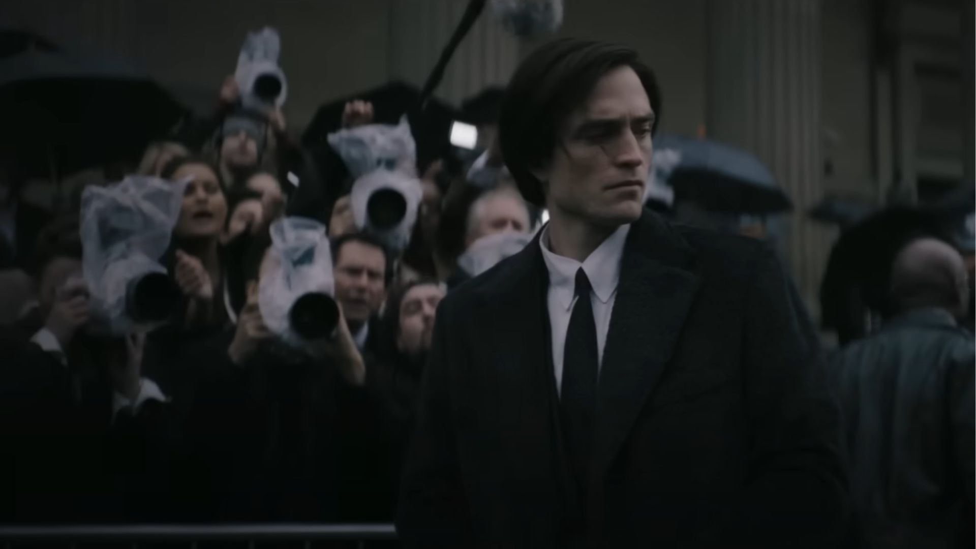 Bruce Wayne (Robert Pattinson) stands serious and watching on his left side