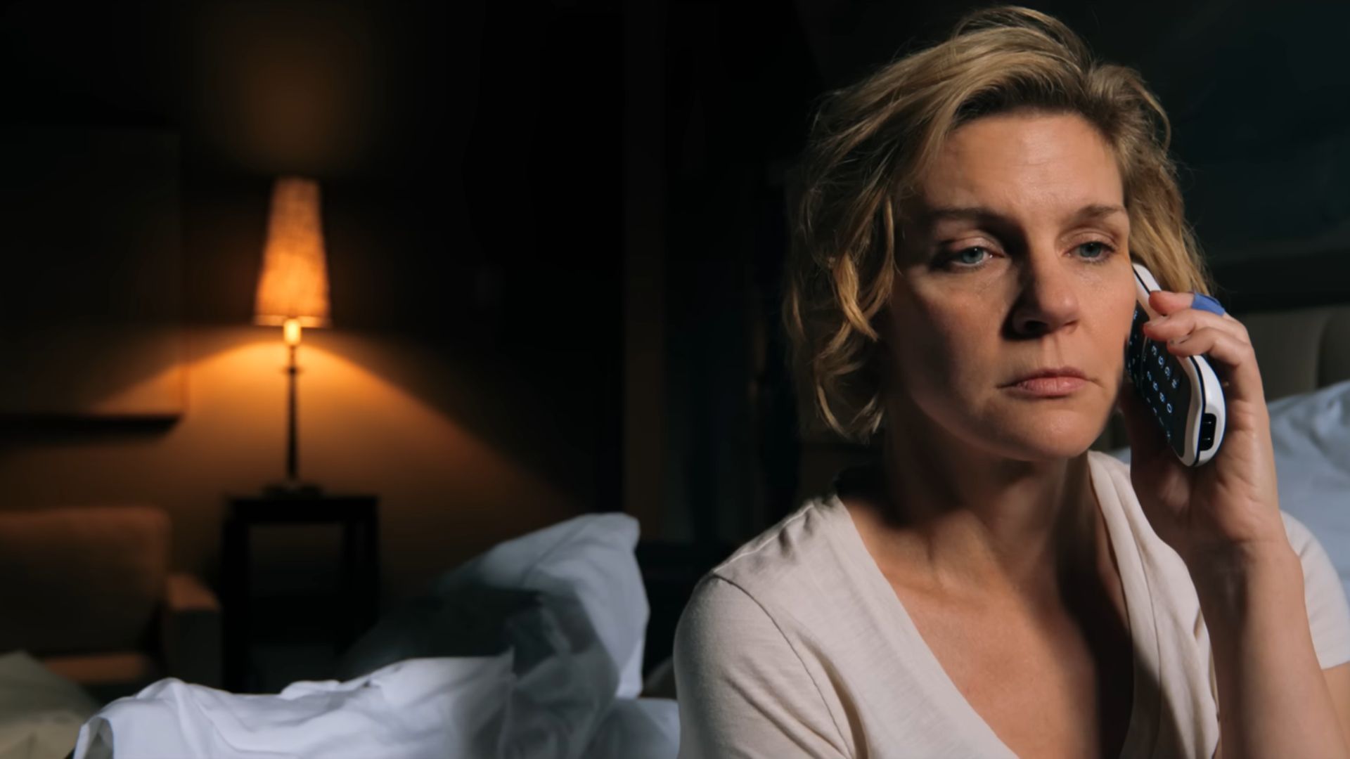 Carol (Rhea Seehorn) is sitting on her bed with a phone in her hand, which is near her ear