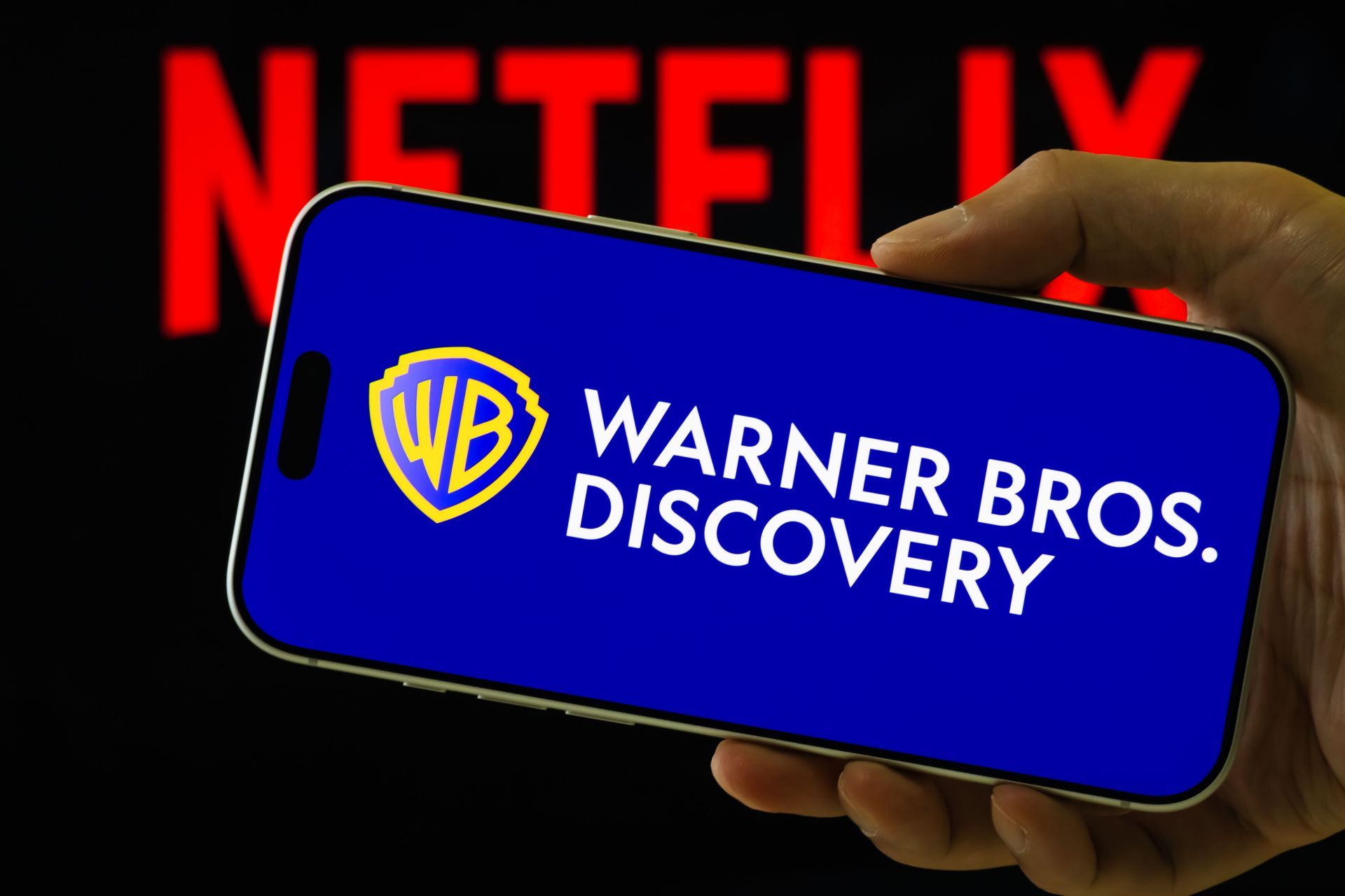 Warner Bros. Discovery Logo Displayed on Smartphone Against Netflix Background - Source: Getty