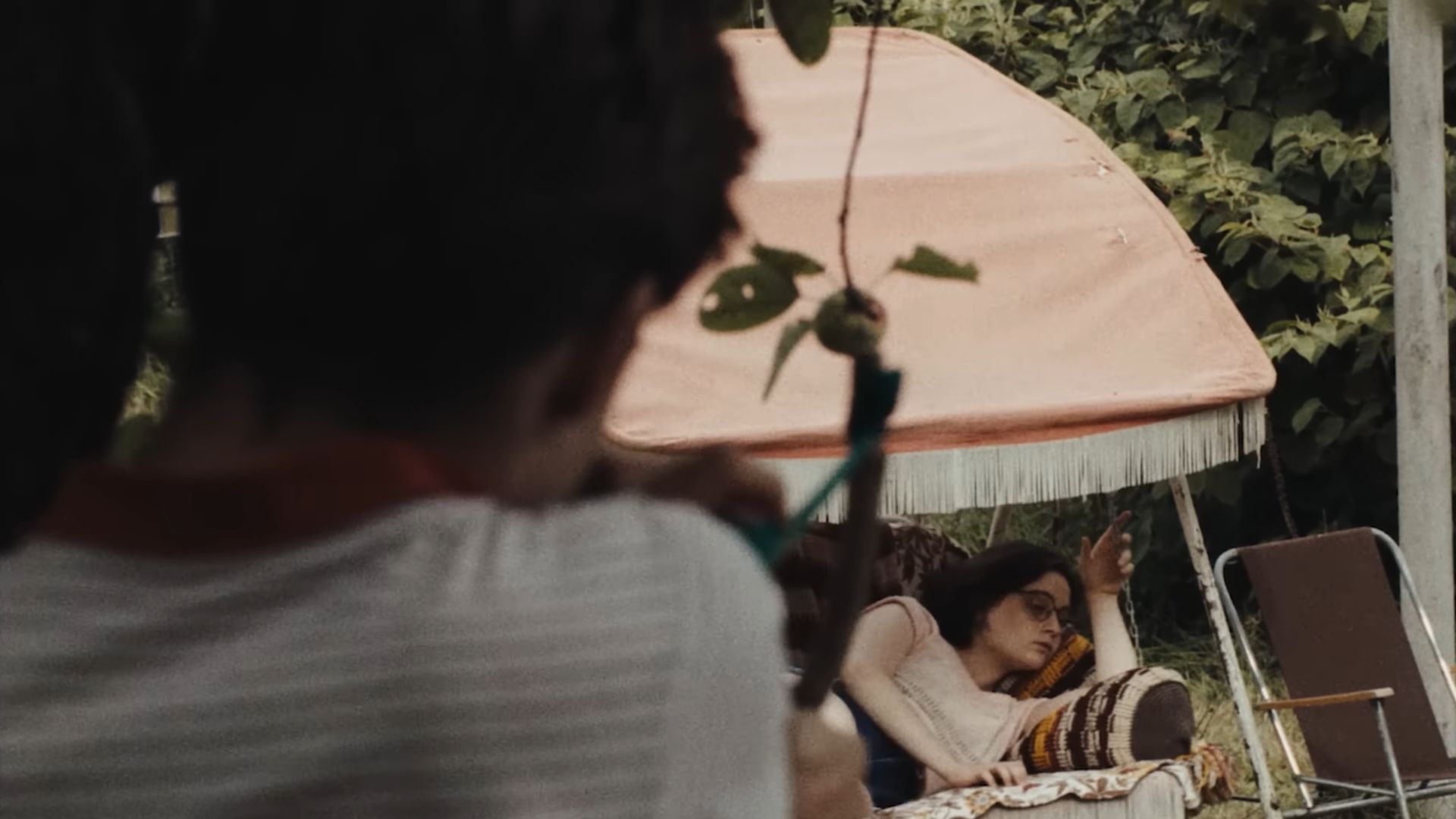 A boy aims at a sleeping girl while she sleeps on a porch swing